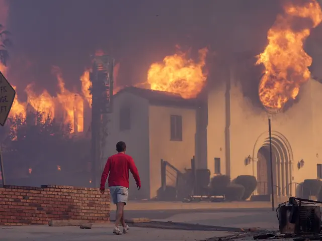 Un hombre camina junto a una Iglesia en llamas en uno de los incendios de Los Ángeles.