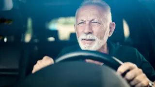 Un hombre mayor conduciendo un vehículo.